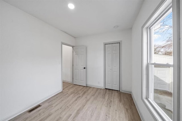 unfurnished bedroom featuring light wood-style floors, visible vents, a closet, and baseboards