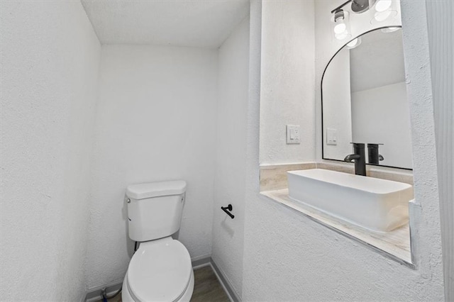 half bathroom with baseboards, toilet, a textured wall, and a sink