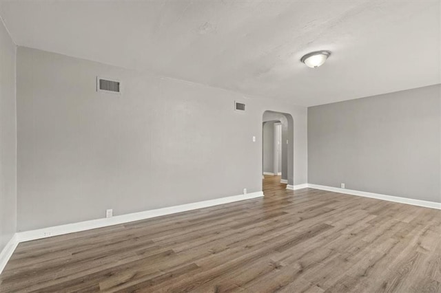 empty room with baseboards, visible vents, arched walkways, and wood finished floors