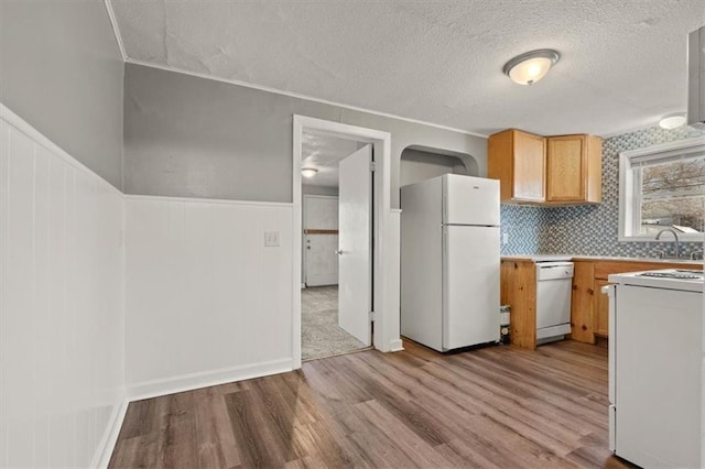 kitchen with a wainscoted wall, light countertops, light wood-style flooring, a textured ceiling, and white appliances