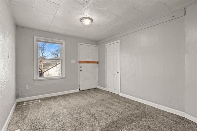 carpeted spare room with a textured wall, visible vents, and baseboards