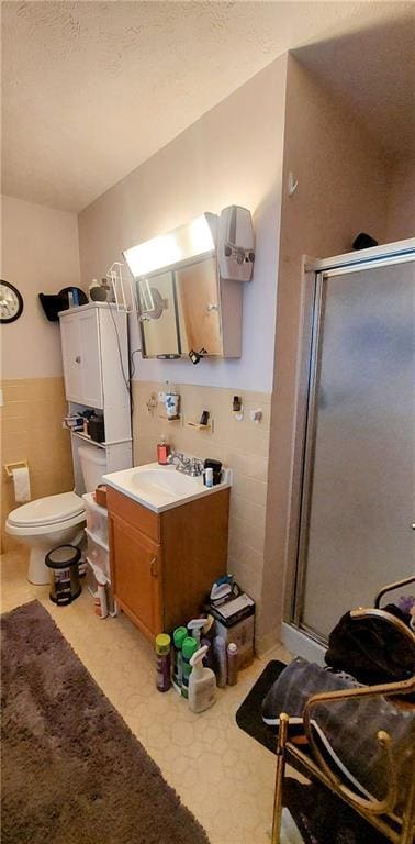 bathroom featuring a stall shower, wainscoting, vanity, and tile walls