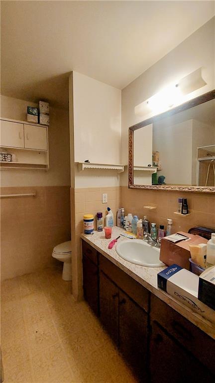 bathroom featuring toilet, a wainscoted wall, vanity, tile walls, and tile patterned floors