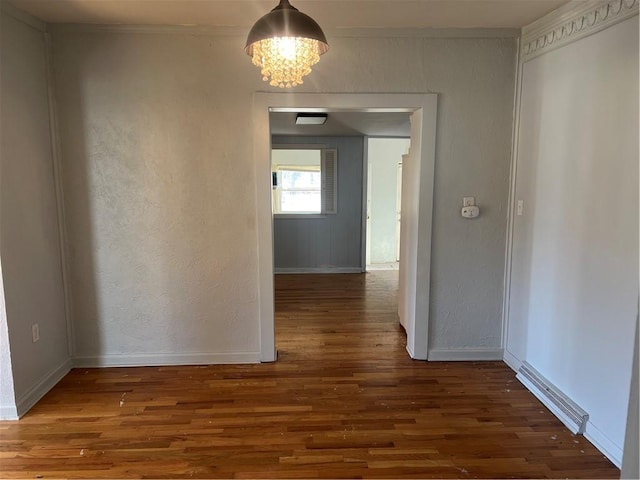 interior space featuring wood finished floors, baseboards, crown molding, a notable chandelier, and a textured wall