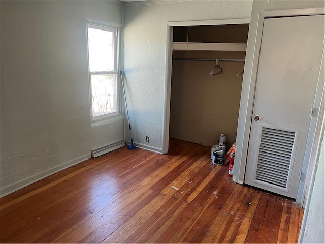 unfurnished bedroom with a baseboard heating unit, wood-type flooring, baseboards, and a textured wall