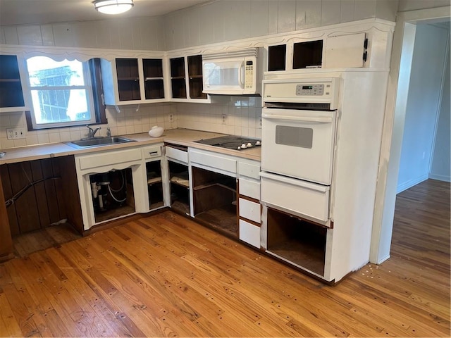 kitchen featuring light wood finished floors, a sink, light countertops, white appliances, and open shelves