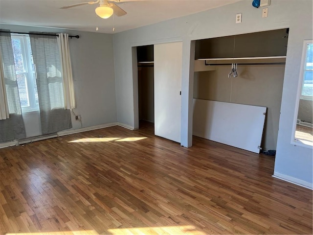 unfurnished bedroom featuring multiple windows, two closets, ceiling fan, and wood finished floors