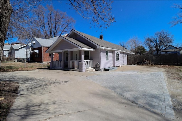 view of front of house featuring a chimney, covered porch, driveway, and fence