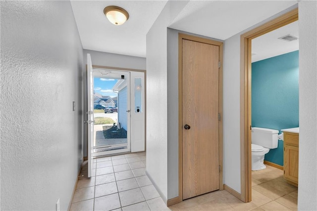 hall featuring light tile patterned floors, visible vents, baseboards, and a textured wall