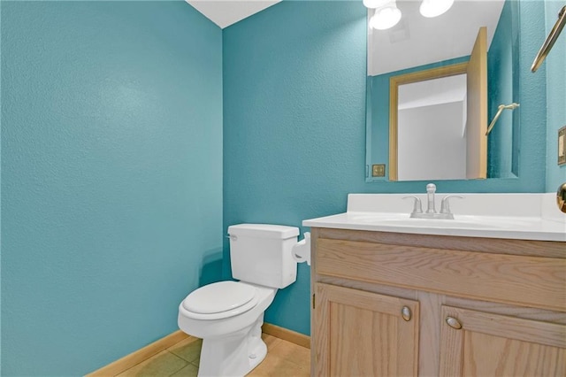 bathroom featuring tile patterned flooring, baseboards, toilet, a textured wall, and vanity