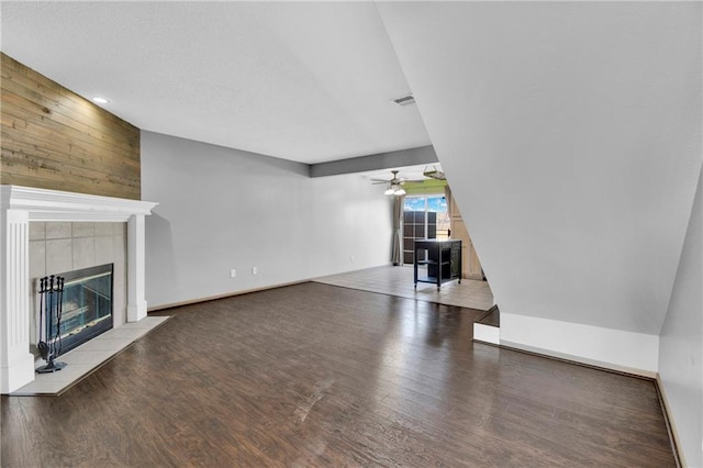 unfurnished living room with a tiled fireplace, wood finished floors, visible vents, and ceiling fan