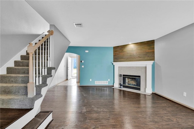 unfurnished living room with a tiled fireplace, visible vents, stairs, and wood finished floors