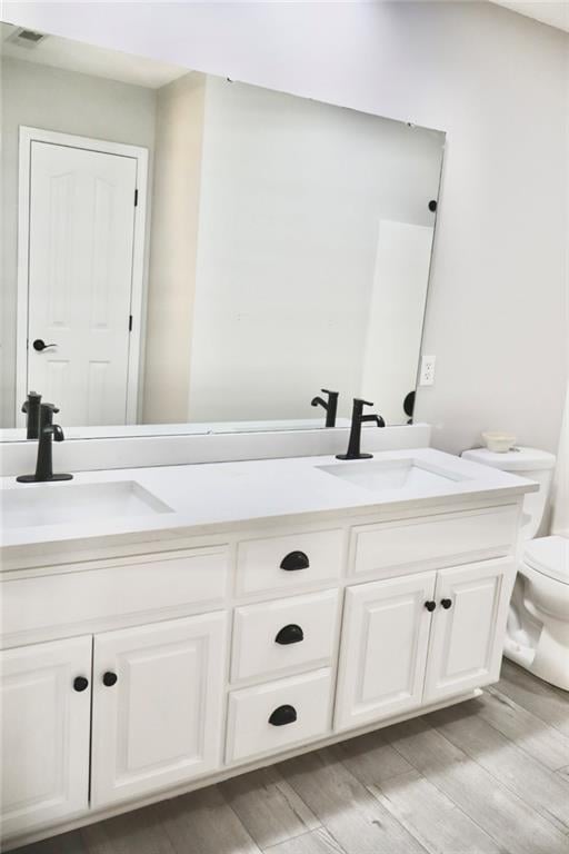 full bathroom with a sink, visible vents, toilet, and double vanity