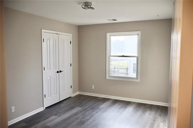 unfurnished bedroom with dark wood-type flooring, visible vents, baseboards, and a closet