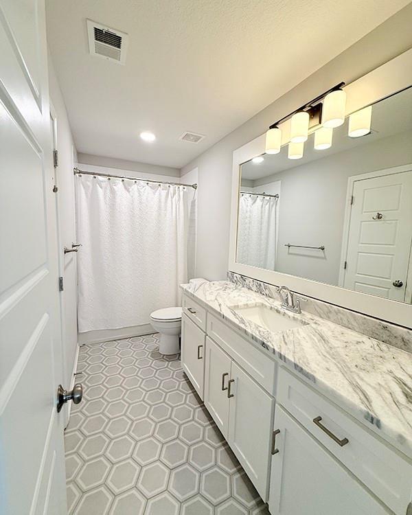 full bathroom featuring toilet, vanity, visible vents, and tile patterned floors