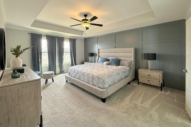 bedroom featuring ceiling fan, light colored carpet, a raised ceiling, and a decorative wall