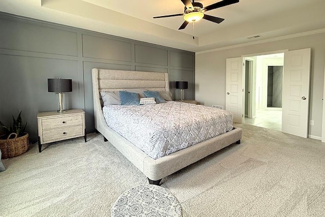 bedroom featuring a tray ceiling, crown molding, visible vents, a decorative wall, and light carpet