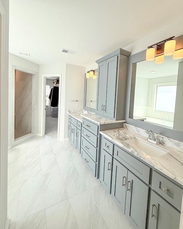 full bath with a textured ceiling, visible vents, two vanities, and a sink