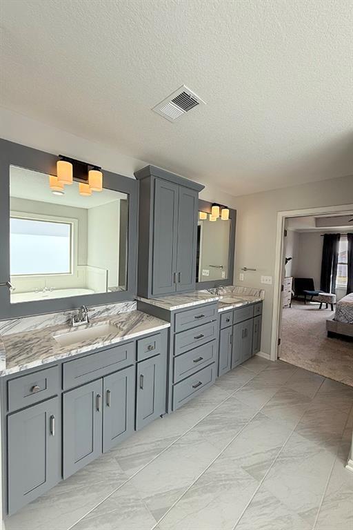 ensuite bathroom featuring two vanities, a sink, visible vents, marble finish floor, and ensuite bath