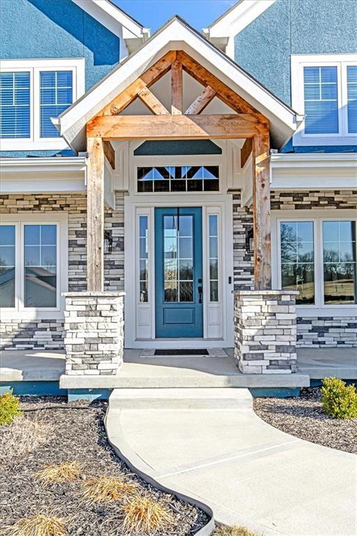 entrance to property featuring covered porch, stone siding, and stucco siding