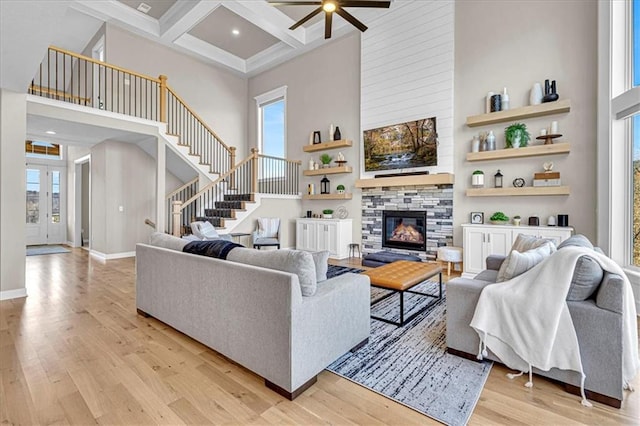 living area with stairs, light wood-type flooring, a towering ceiling, and a large fireplace