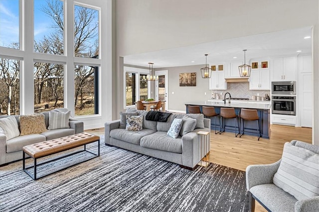 living room featuring baseboards, recessed lighting, a high ceiling, light wood-style floors, and a notable chandelier