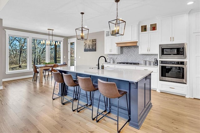 kitchen with backsplash, light countertops, appliances with stainless steel finishes, white cabinets, and a kitchen island with sink