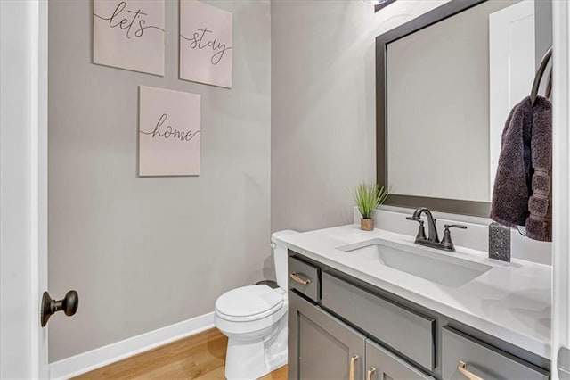 half bath with toilet, vanity, baseboards, and wood finished floors