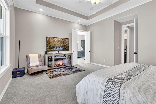 bedroom featuring a tray ceiling, baseboards, a glass covered fireplace, and carpet flooring