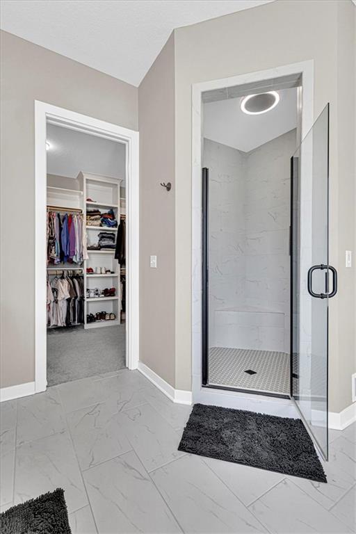 bathroom with a spacious closet, marble finish floor, a stall shower, and baseboards