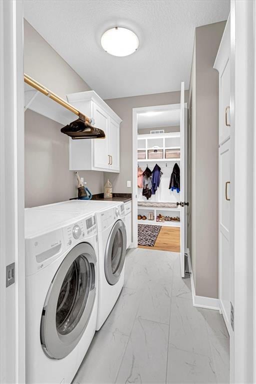 clothes washing area with marble finish floor, a textured ceiling, cabinet space, separate washer and dryer, and baseboards