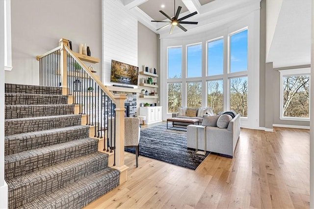 living area with stairway, hardwood / wood-style floors, a stone fireplace, a high ceiling, and coffered ceiling