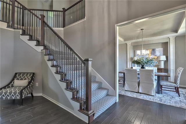 stairway featuring baseboards, decorative columns, wood finished floors, a notable chandelier, and a raised ceiling