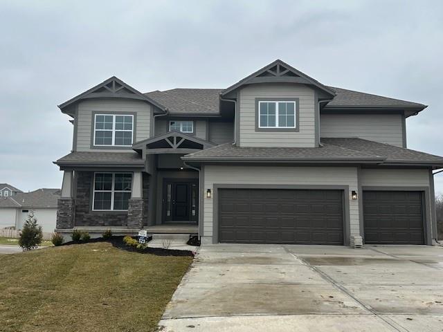 view of front of home with roof with shingles, an attached garage, concrete driveway, a front lawn, and stone siding