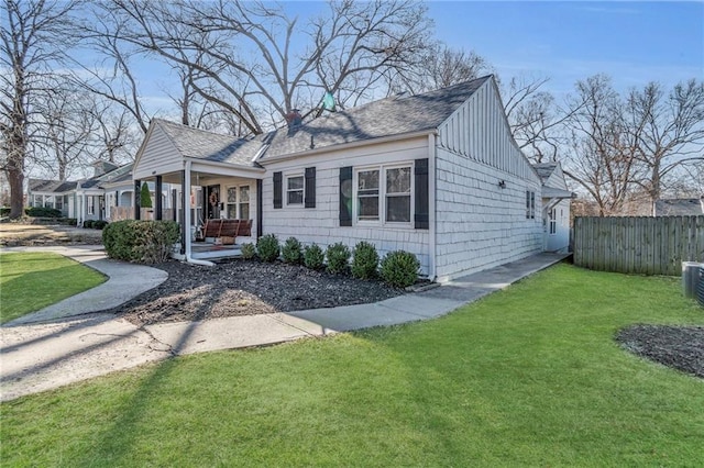 bungalow-style home featuring roof with shingles, covered porch, a front yard, and fence