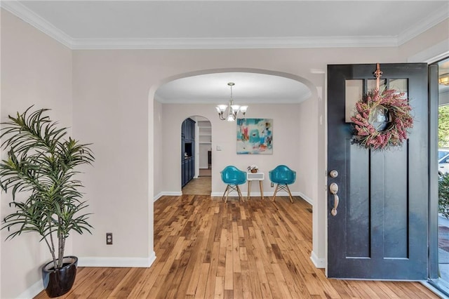 foyer entrance featuring baseboards, arched walkways, light wood finished floors, and ornamental molding