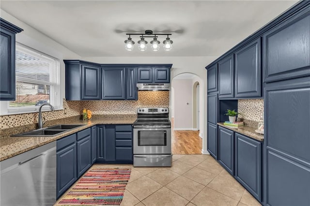 kitchen with a sink, under cabinet range hood, arched walkways, appliances with stainless steel finishes, and light tile patterned floors