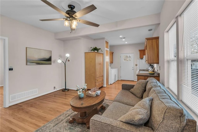 living area with visible vents, light wood-type flooring, washer and dryer, baseboards, and ceiling fan