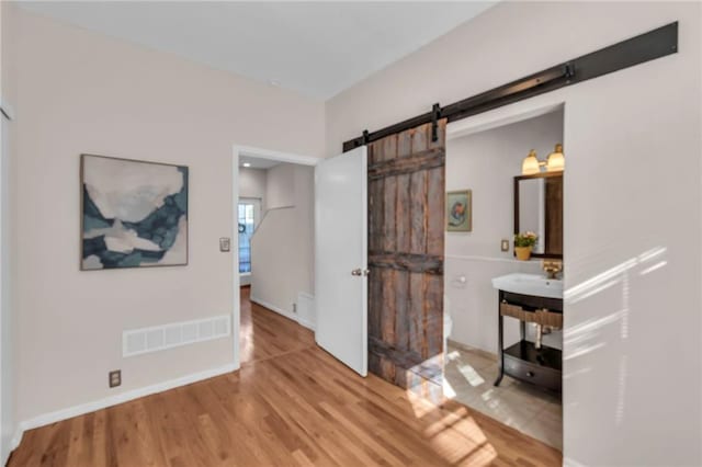 interior space featuring a barn door, baseboards, visible vents, and wood finished floors