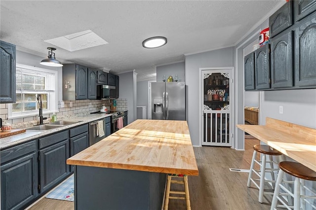 kitchen featuring a breakfast bar area, a skylight, stainless steel appliances, wood counters, and a sink