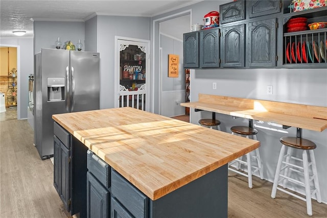 kitchen featuring light wood-style flooring, ornamental molding, butcher block countertops, stainless steel refrigerator with ice dispenser, and a kitchen bar