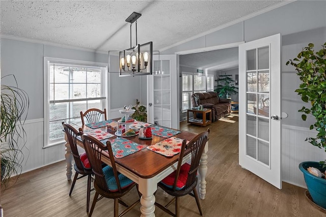 dining room featuring a wainscoted wall, a textured ceiling, wood finished floors, french doors, and vaulted ceiling