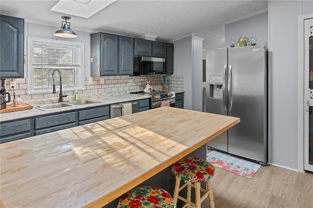 kitchen featuring light wood finished floors, a skylight, a sink, appliances with stainless steel finishes, and wood counters