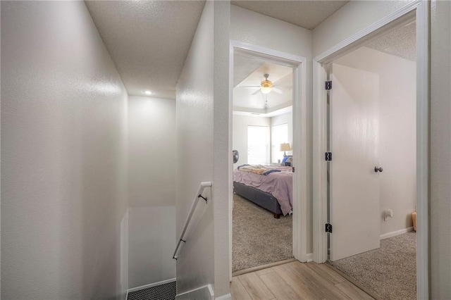 corridor with an upstairs landing, light carpet, light wood-style floors, and a textured wall