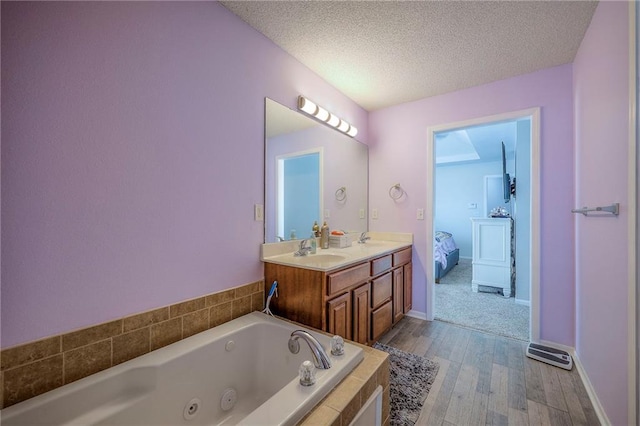 full bathroom with a sink, a textured ceiling, a tub with jets, and ensuite bathroom