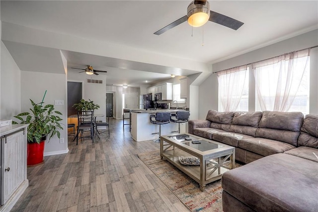 living area featuring baseboards, wood finished floors, visible vents, and ceiling fan