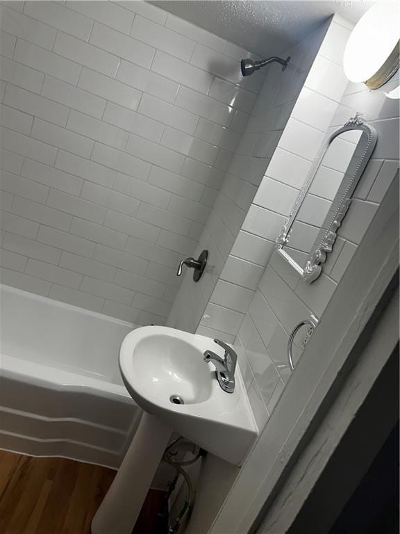 full bath featuring a textured ceiling, wood finished floors, shower / tub combination, and a sink