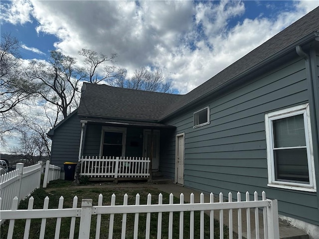 exterior space with a fenced front yard, a porch, and roof with shingles