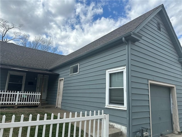 view of side of property with a fenced front yard, covered porch, a garage, and roof with shingles