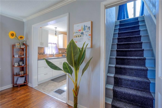 stairs featuring crown molding, wood finished floors, baseboards, and visible vents